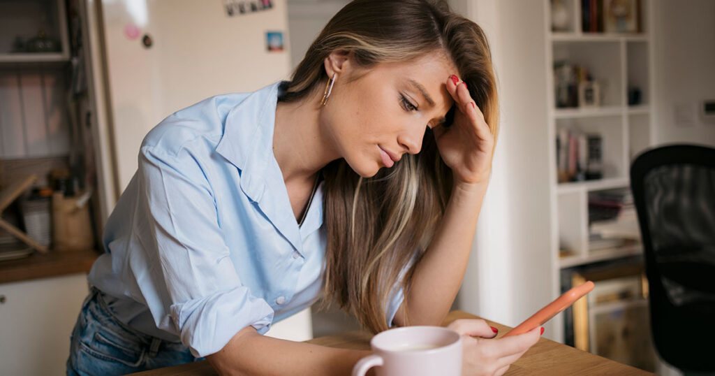 Woman frustrated with her hand on her head and looking at her cell phone.